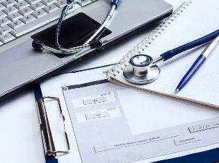 A stethoscope on top of documents and a laptop.