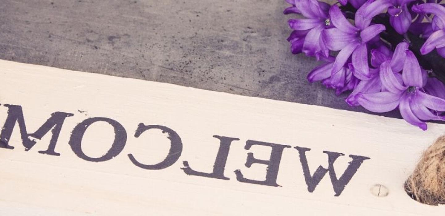 Welcome plaque on the ground with purple flowers